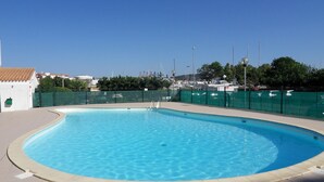 Una piscina con borde curvo, rodeada por una valla verde y una zona de terraza con baldosas.