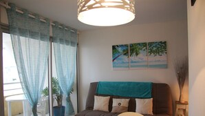 Una sala de estar con un sofá, una mesa de comedor, una planta en maceta y un cuadro en la pared.