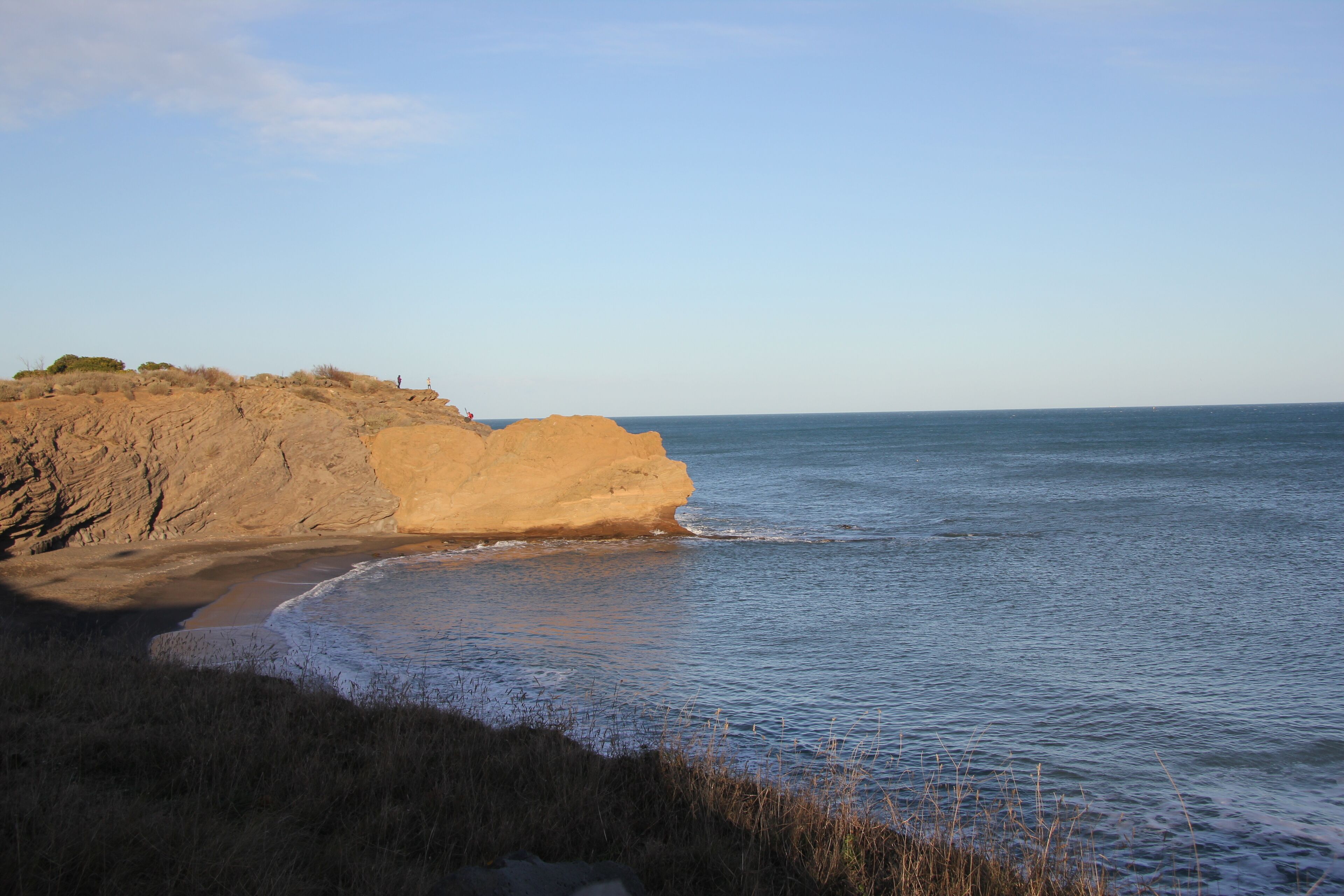 A coastal landscape with a sandy beach, rocky cliffs, and a clear sky.