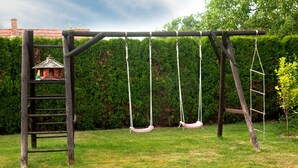 A wooden swing set with a ladder and a birdhouse in a grassy backyard.