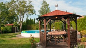 A wooden gazebo with a red roof, a pool, and a well-maintained garden.