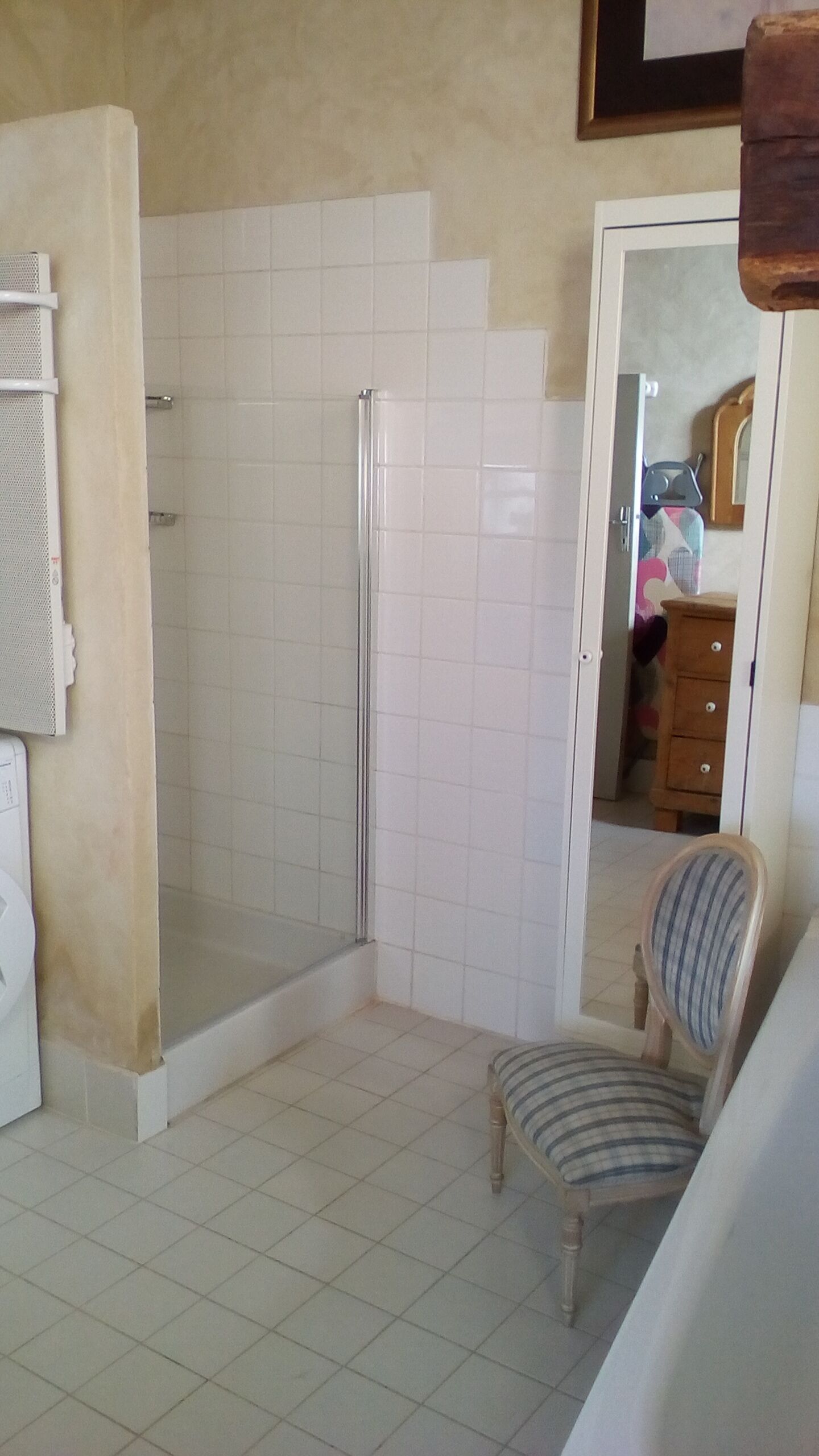 Een badkamer met een douche, wastafel en een stoel.