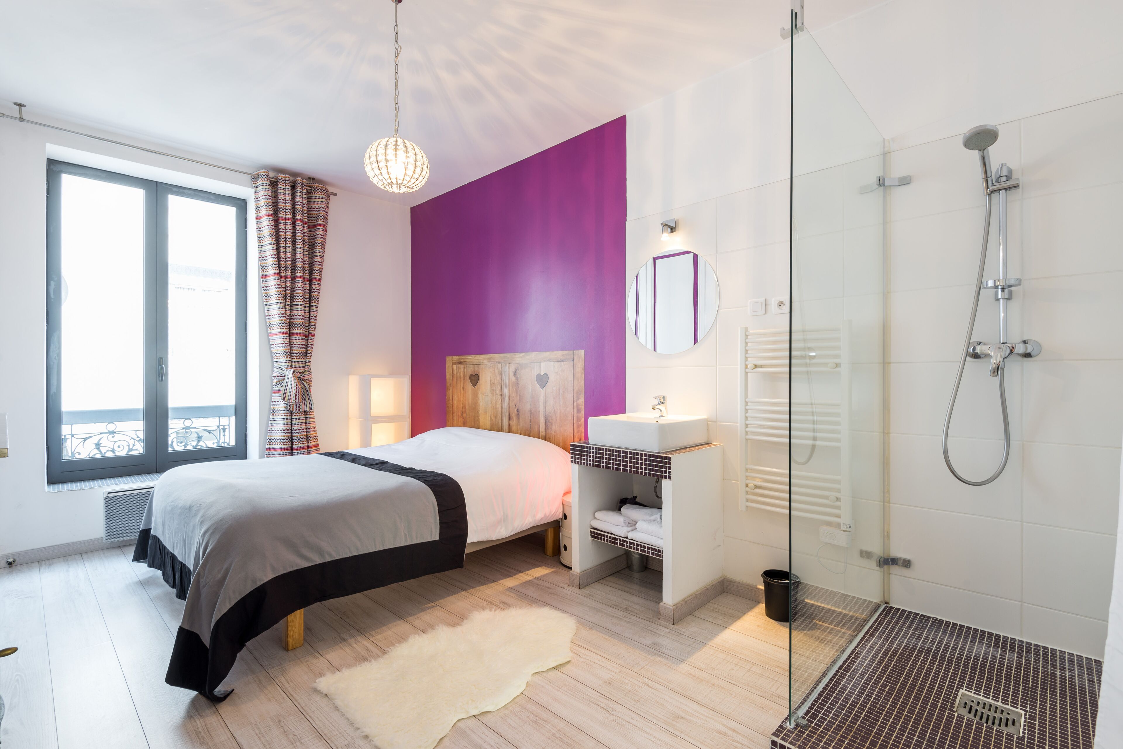 A modern bedroom with a bed, a bathroom with a shower, and a window with curtains.