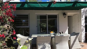 A covered patio with wicker furniture, a table with a bowl of fruit, and a potted plant. - Family-friendly, sunny holiday home with pool, splendid views and solar power (Cape Town)