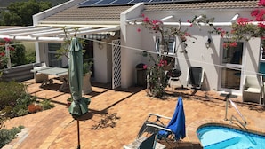 A pool area with a chair and umbrella, a pergola, and solar panels on the roof. - Family-friendly, sunny holiday home with pool, splendid views and solar power (Cape Town)