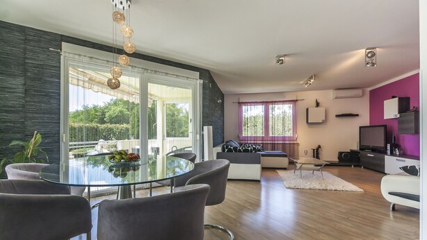 Una sala de estar moderna con una mesa de comedor de cristal, sillas tapizadas en gris, un sofá y una televisión.