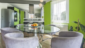 Una cocina moderna con una mesa de comedor de vidrio, sillas tapizadas en gris y un frutero.