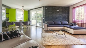 Una sala moderna con un sofá modular, un comedor con sillas y una cocina al fondo.