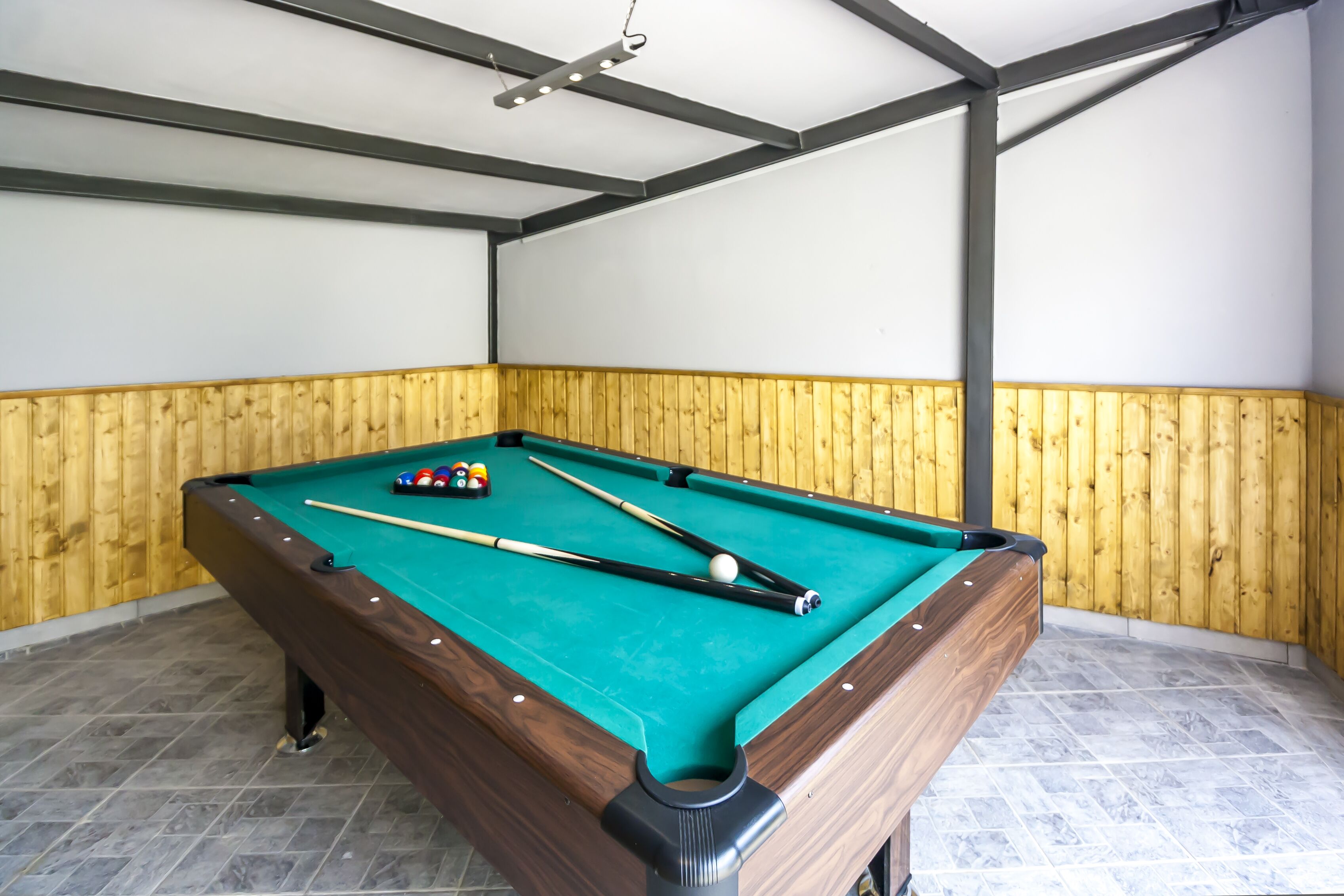 A pool table with balls and cues, wooden paneling on the walls, and a tiled floor.