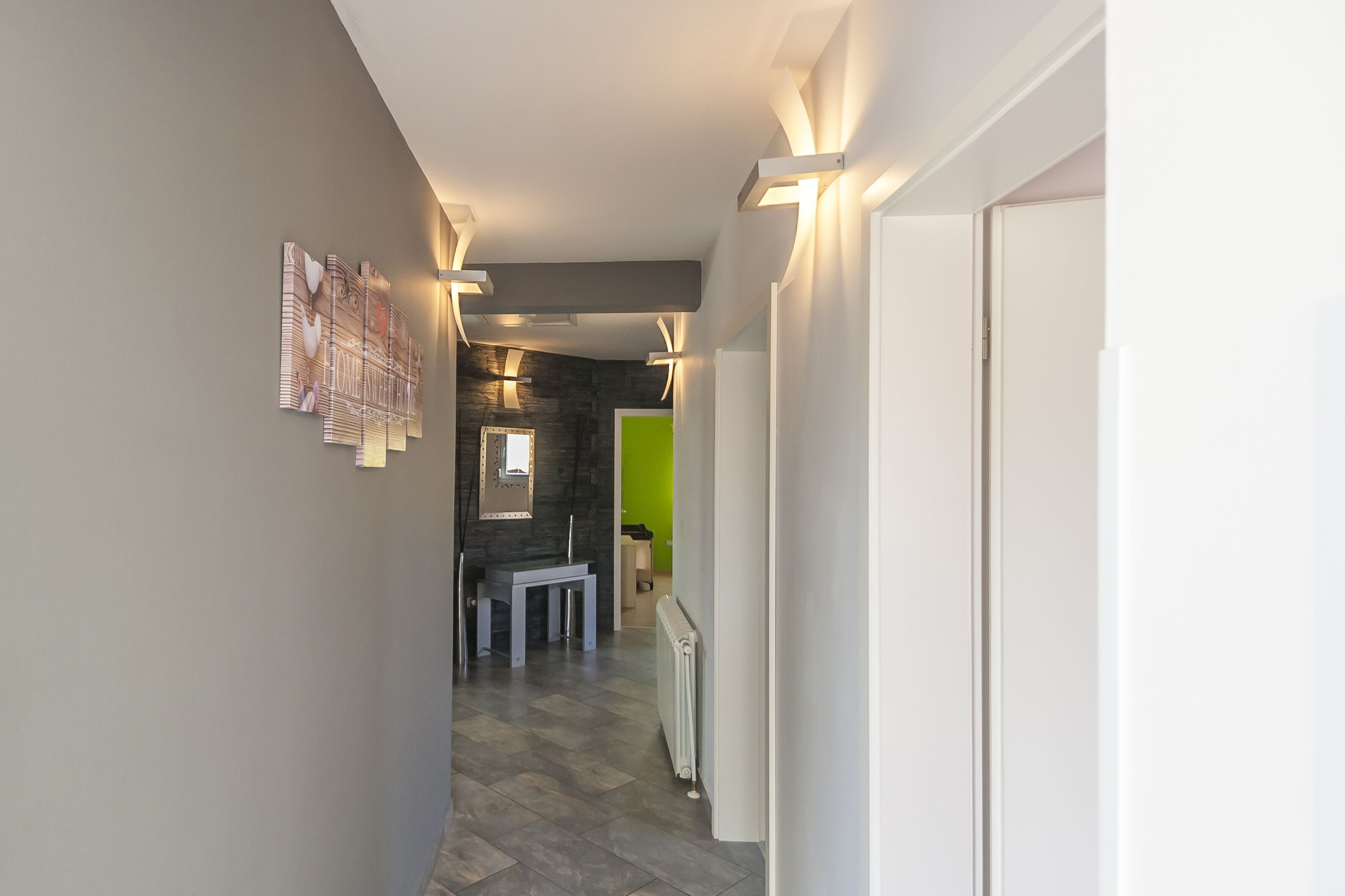 A hallway with a modern design, featuring a bench, a radiator, and a green wall in the background.