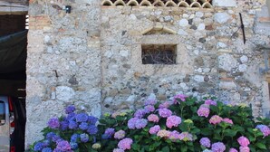 Un edificio de piedra con un ventanal de tejas y un macizo de hortensias.