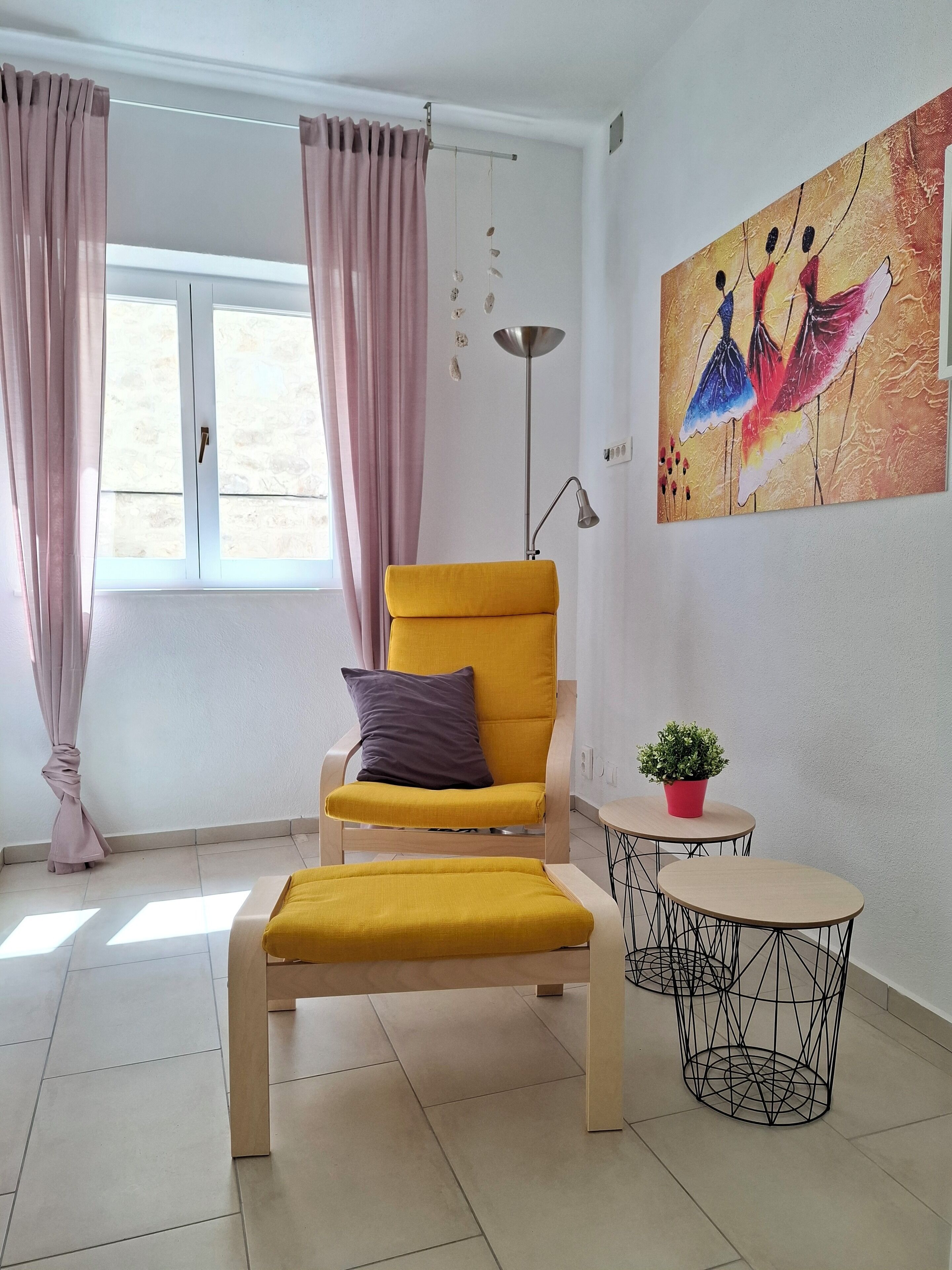 Una habitación con un sillón amarillo, una mesita redonda con una planta en maceta y un cuadro en la pared.