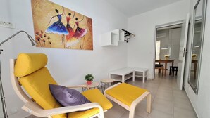 Een moderne woonkamer met een gele fauteuil, een bijzettafeltje met een plant in pot en een schilderij aan de muur.