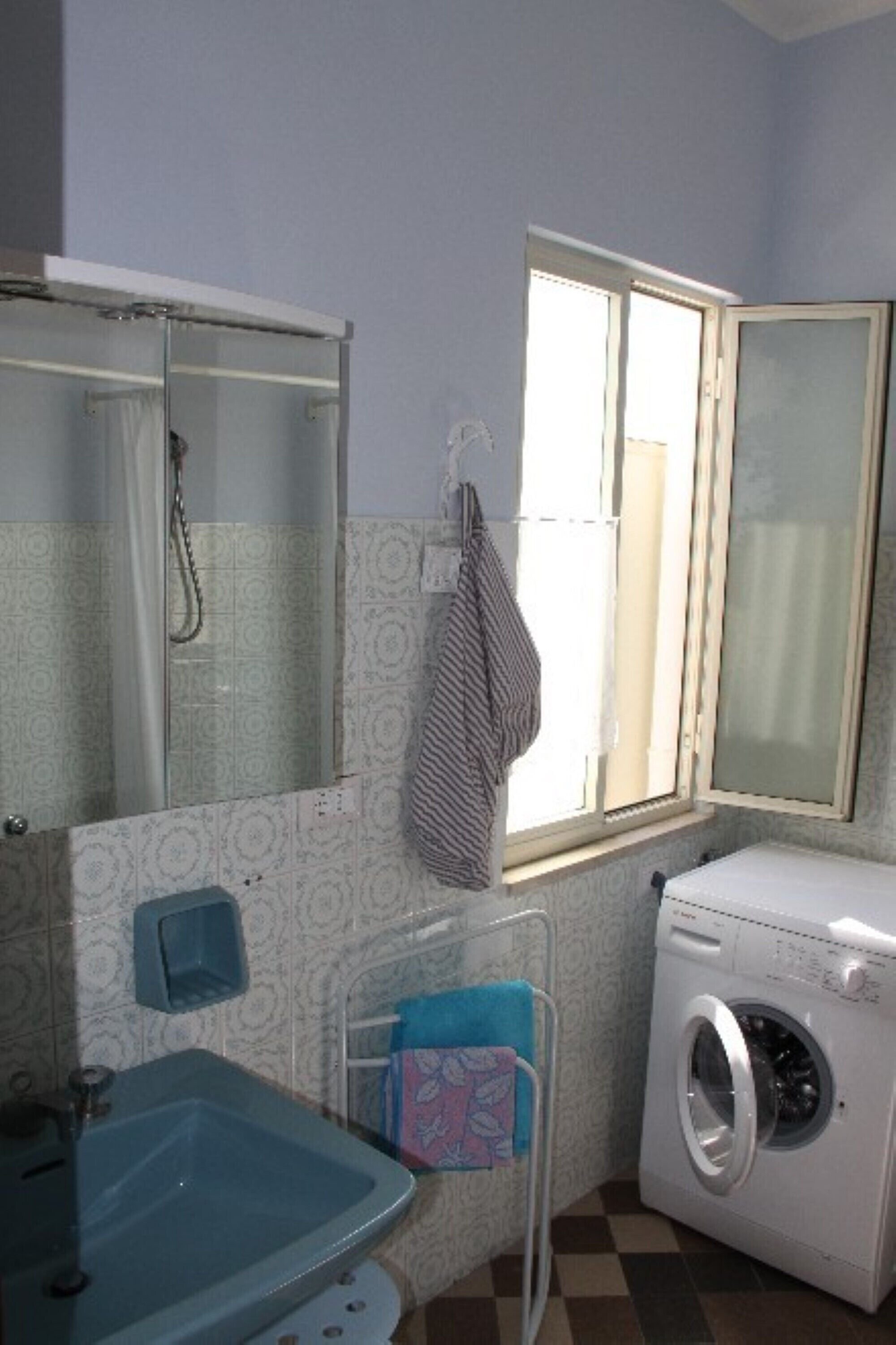 Un baño con lavamanos, espejo, ventana y lavadora.
