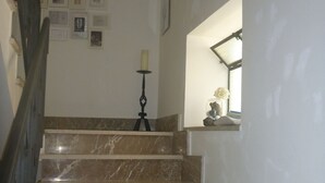 Una scala in marmo con ringhiera, un lampadario a parete e un quadro incorniciato.