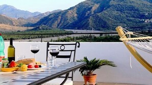Un tavolo apparecchiato all'aperto con vista sulle montagne, un'amaca e una pianta in vaso.