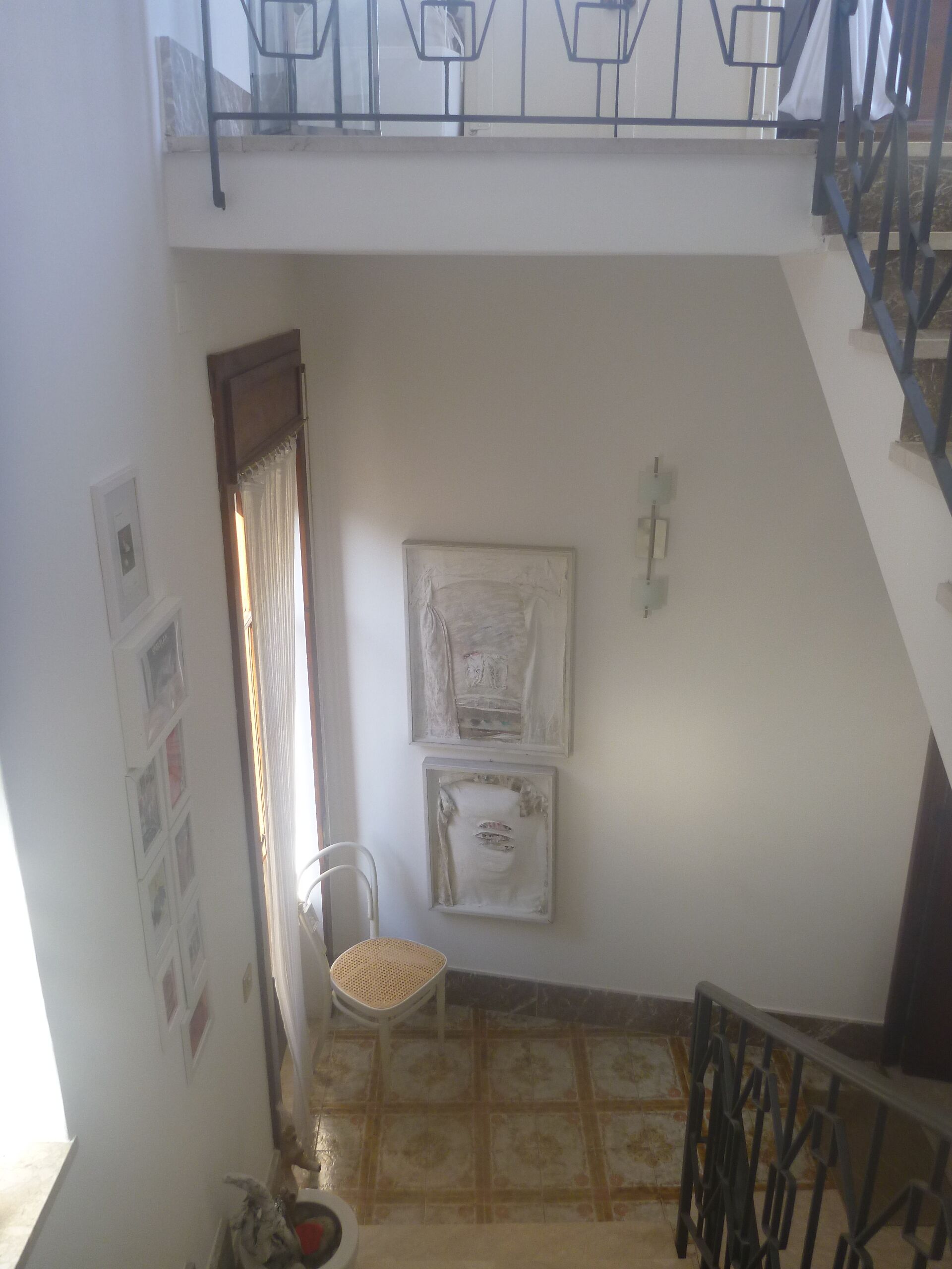 A small, enclosed balcony with a metal railing, a chair, and a tiled floor.