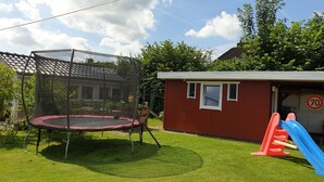 Ein Trampolin in einem Garten mit einem kleinen roten Schuppen und einer blauen Rutsche.