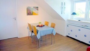 Ein Essbereich mit einem Tisch für sechs Personen, einem Fenster mit Jalousien und einer Küche mit blauen Schränken.