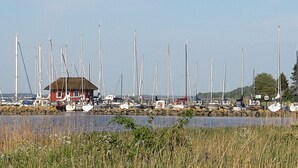 Ein Hafen mit mehreren Segelbooten, ein kleines Gebäude und eine natürliche Landschaft im Hintergrund.