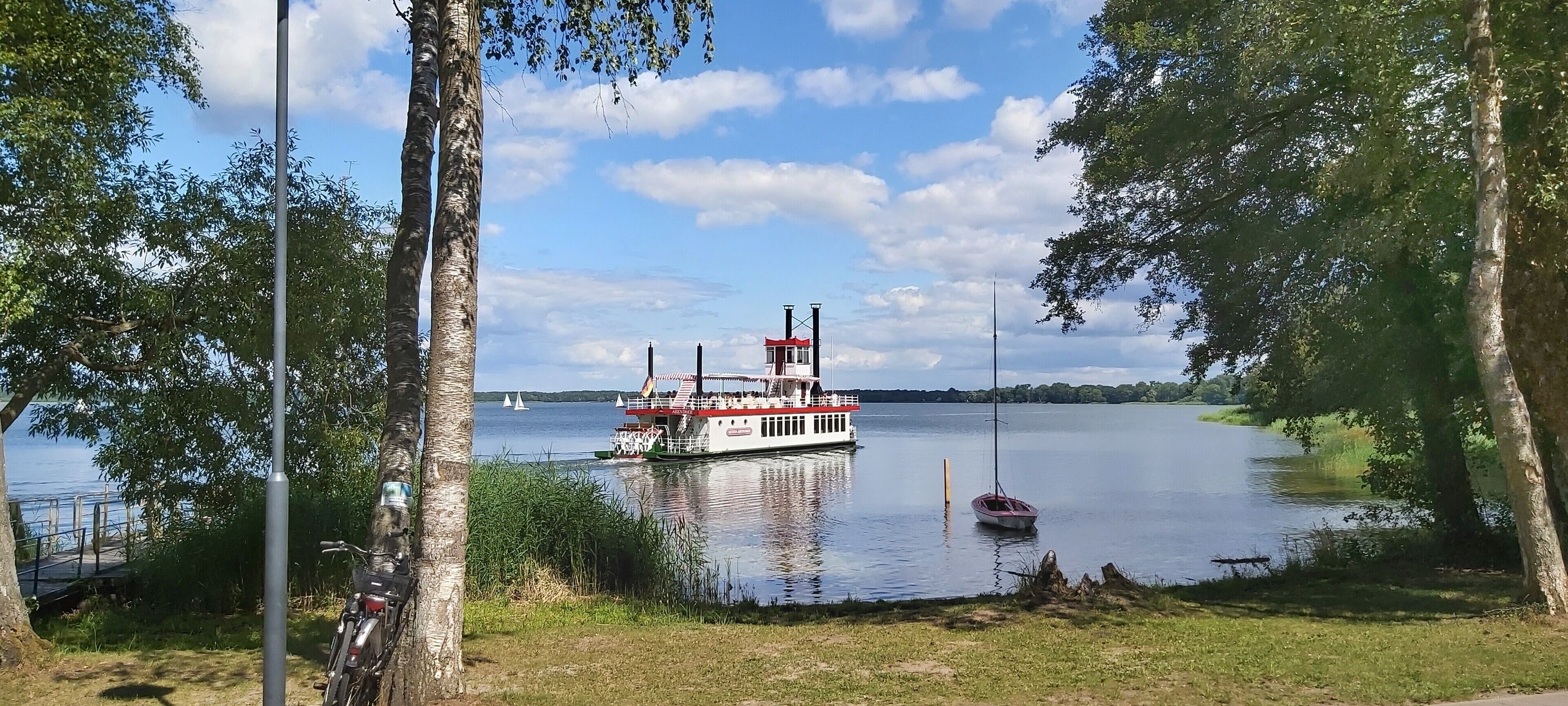 A lake with a white boat docked near the shore, surrounded by trees and a clear sky.