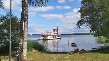 A lake with a white boat docked near the shore, surrounded by trees and a clear sky.