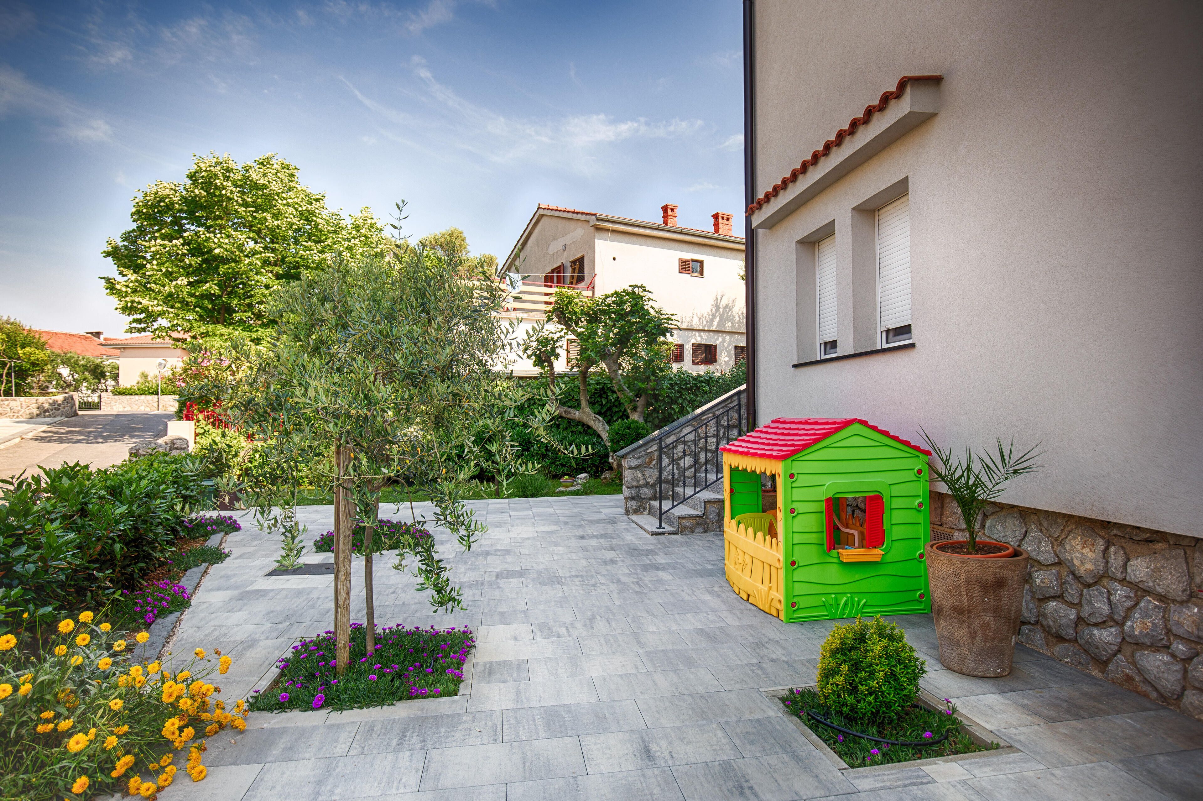 A courtyard with a playhouse, a tree, and a stone wall.