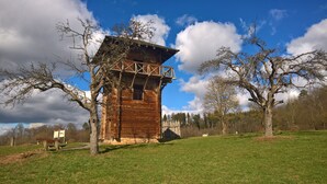 Une tour en bois dotée d’un balcon, entourée d’arbres et bordée d’une pelouse.