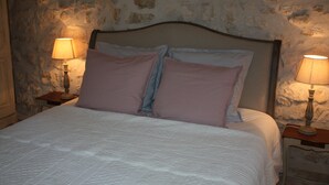Een bed met hoofdeinde, twee nachtkastjes met lampen en een stenen muur.