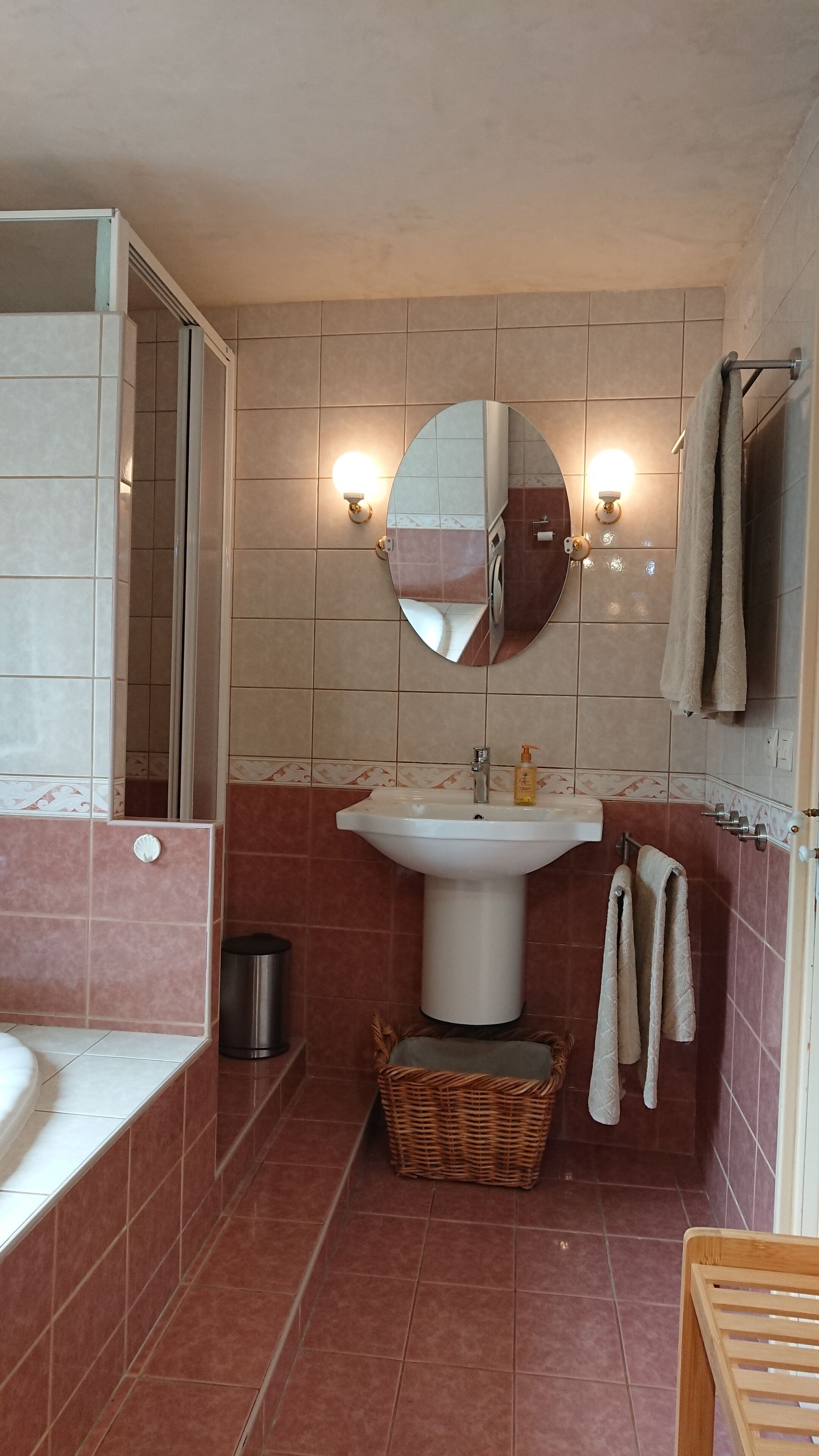 Une salle de bain avec un lavabo blanc, un miroir, un porte-serviettes et un panier en osier.