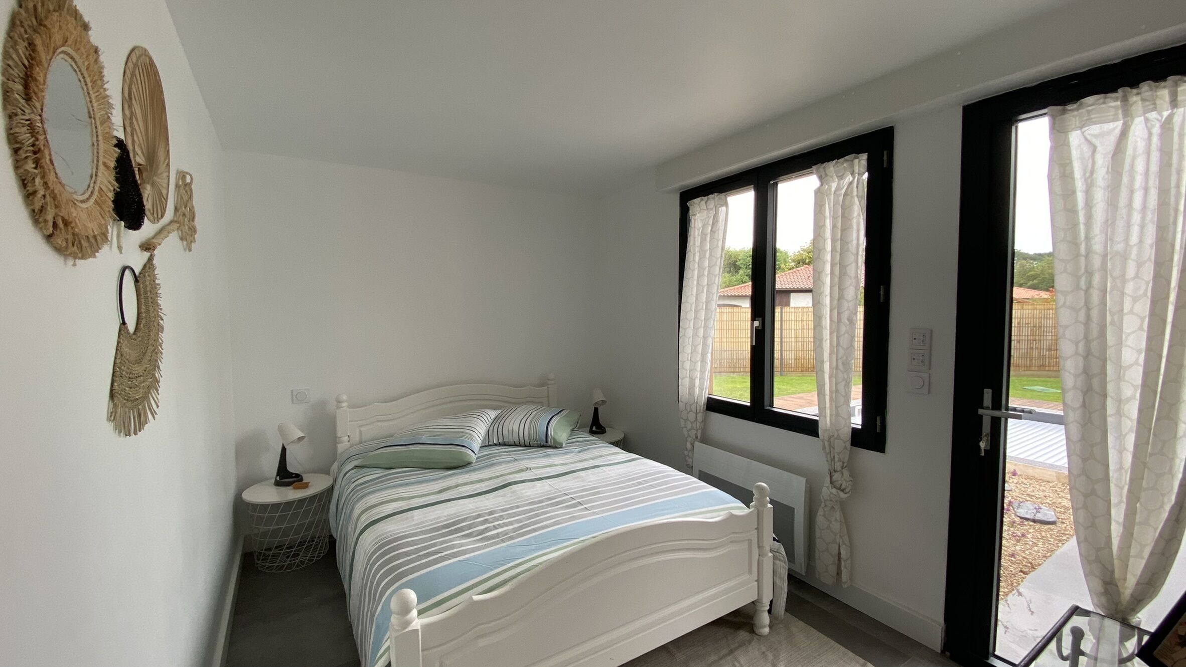Une chambre à coucher avec un lit, des tables de chevet, une fenêtre avec des rideaux et une vue sur l’extérieur.