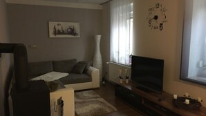 Ett vardagsrum med en grå soffa, en vit fåtölj, en tv på ett träställ och en tavla på väggen.