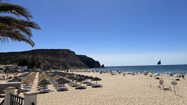 A beach with rows of sun umbrellas and lounge chairs, a flag, and a mountainous backdrop. - Vila Marquês da Luz, ideal villa for guests looking for peace and quiet, sea view 1 floor (Luz)