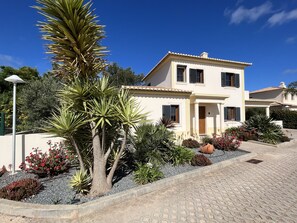 A two-story house with a tiled roof, a paved driveway, and a variety of plants and shrubs in the garden area.