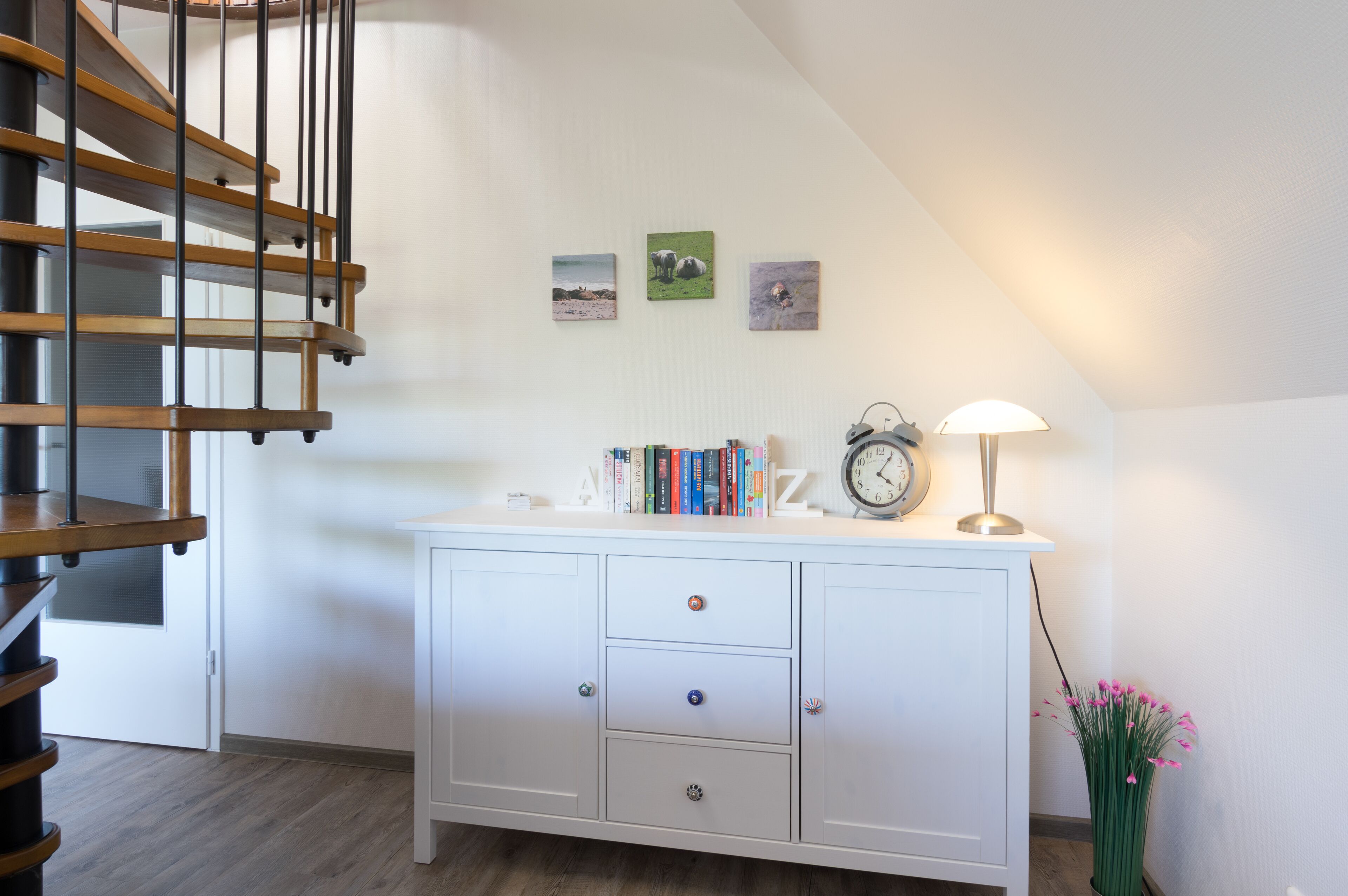 A staircase with wooden steps and a white wall with three framed pictures.