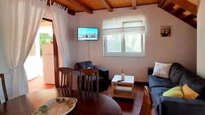 A cozy living room with a wooden ceiling, a television mounted on the wall, a sofa, a dining table with chairs, and a window with curtains. - Family-friendly country house Marie with heated pool, barbecue area, 5 persons (Krk)