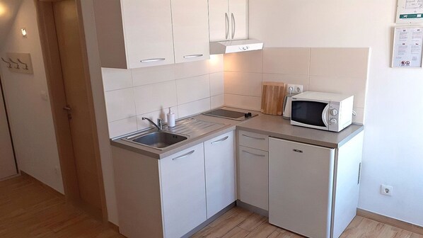 Una cocina compacta con armarios blancos, microondas integrado y un lavamanos.