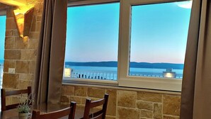 A room with stone walls, a wooden table, and a view of a body of water through a window with curtains. - Holiday apartment "Villa Bonaca" with a beautiful panoramic (Baska Voda)