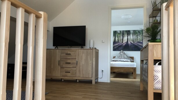 A modern bedroom with a wooden wardrobe, a bed with patterned pillows, a television on the wall, and a large forest-themed painting. - Wendlers Ferienwohnungen 4-6 (Schwaig bei Nuernberg)