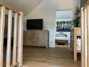 A modern bedroom with a wooden wardrobe, a bed with patterned pillows, a television on the wall, and a large forest-themed painting. - Wendlers Ferienwohnungen 4-6 (Schwaig bei Nuernberg)