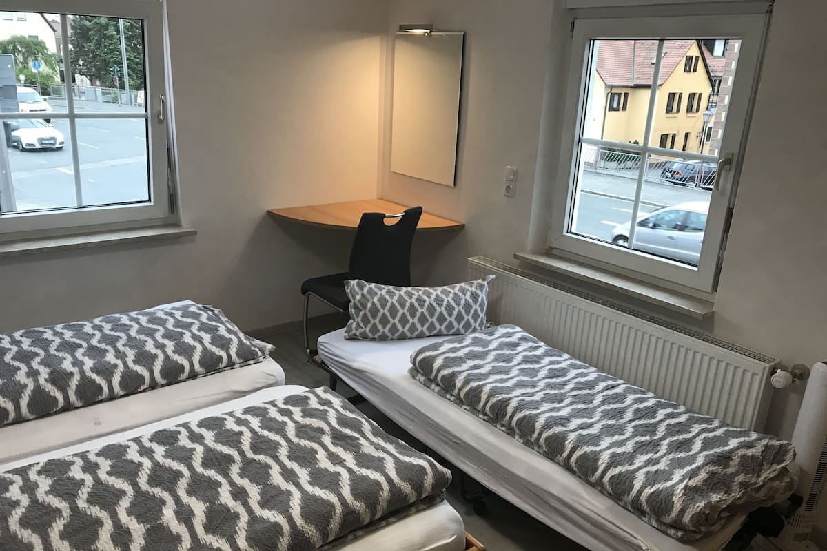 Ein kleines Zimmer mit zwei Einzelbetten, einem Schreibtisch, einem Stuhl und einem Fenster zur Straße hinaus.