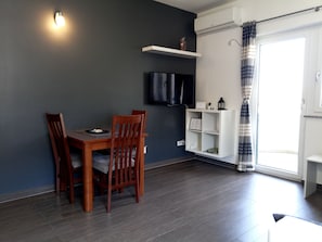 Un coin repas avec une table et des chaises, un téléviseur fixé au mur et une étagère blanche.