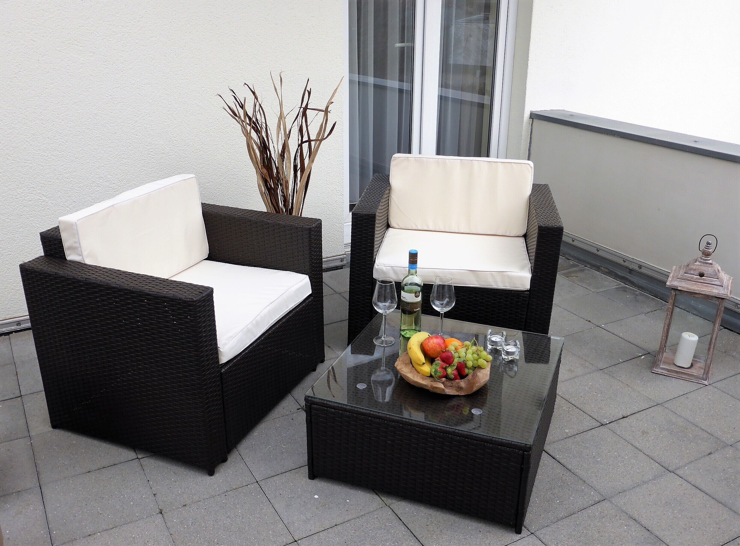 A patio with wicker furniture, a glass table with fruit and wine glasses, and a lantern.