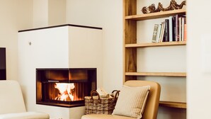 Ein gemütliches Wohnzimmer mit Kamin, einer bequemen Couch, einem Bücherregal und einem Korbwannenmöbel.