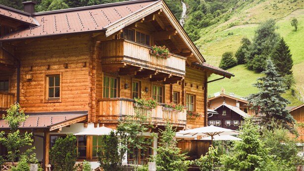 Eine Holzhütte mit Balkon, umgeben von üppiger Vegetation und einer Berglandschaft.