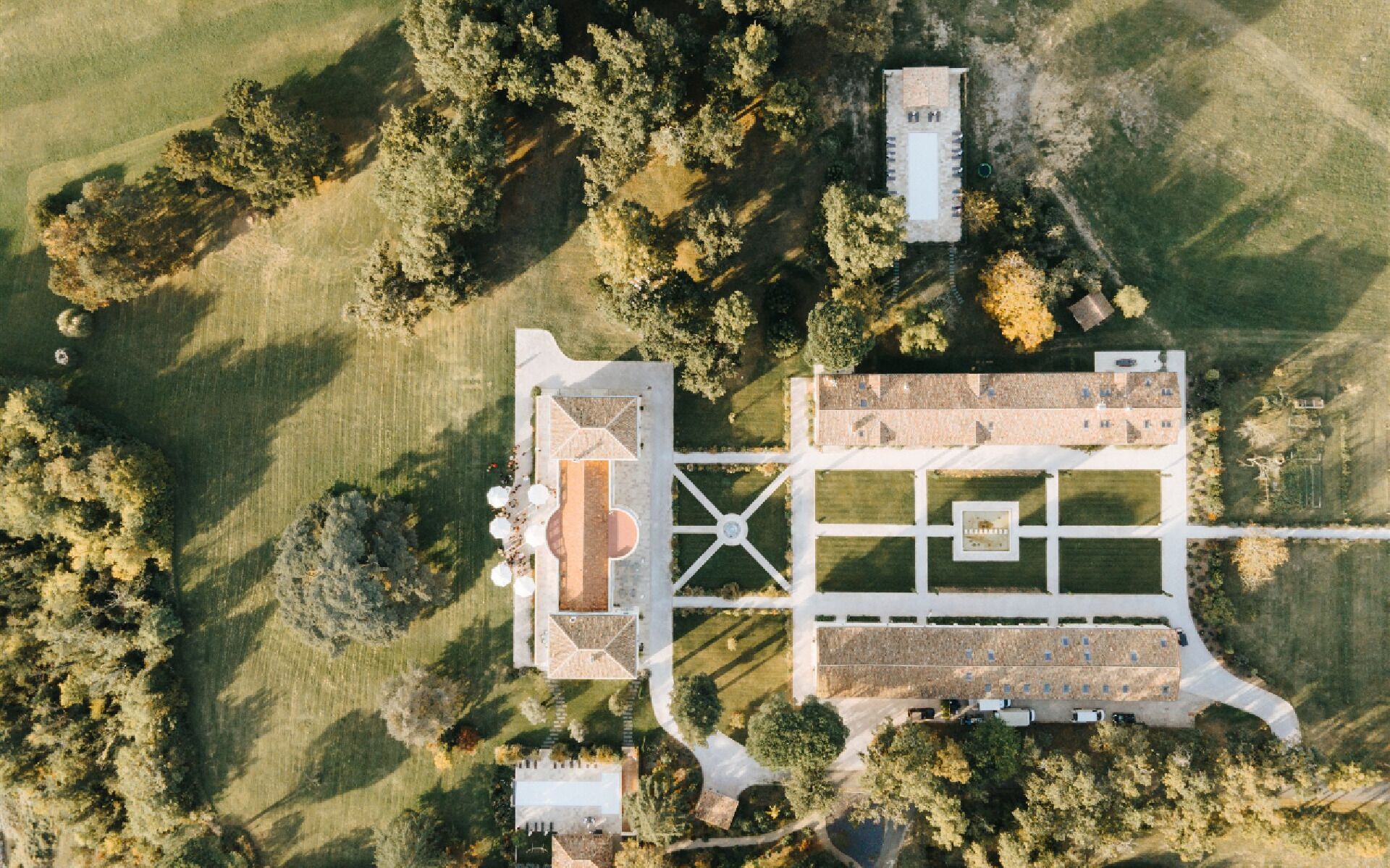 An aerial view of a property with a central courtyard, surrounding buildings, and a parking area.