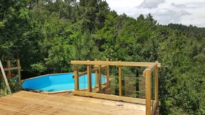 Una terraza de madera con una piscina azul rodeada de bosque denso.