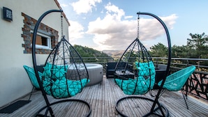 Una terraza de madera con sillas colgantes y una mesa, con vistas a un paisaje pintoresco.