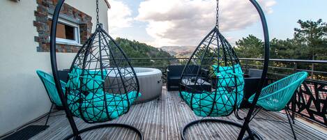 Une terrasse en bois avec des fauteuils suspendus et une table, offrant une vue imprenable sur un paysage magnifique.