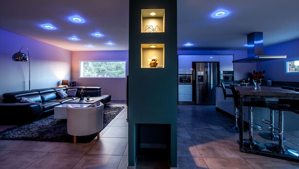 Una sala de estar moderna con un sofá de cuero negro, una mesa de centro blanca y una mesa de comedor de vidrio con taburetes de bar.